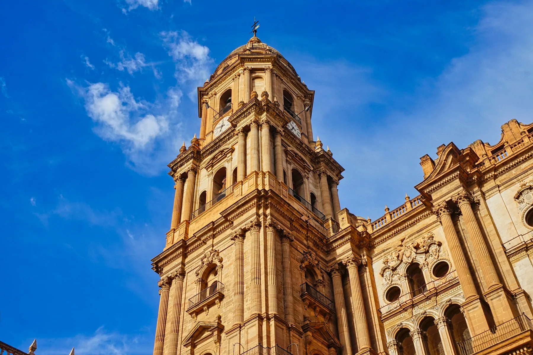 The bell tower and carved façade of Málaga Cathedral against a bright blue sky